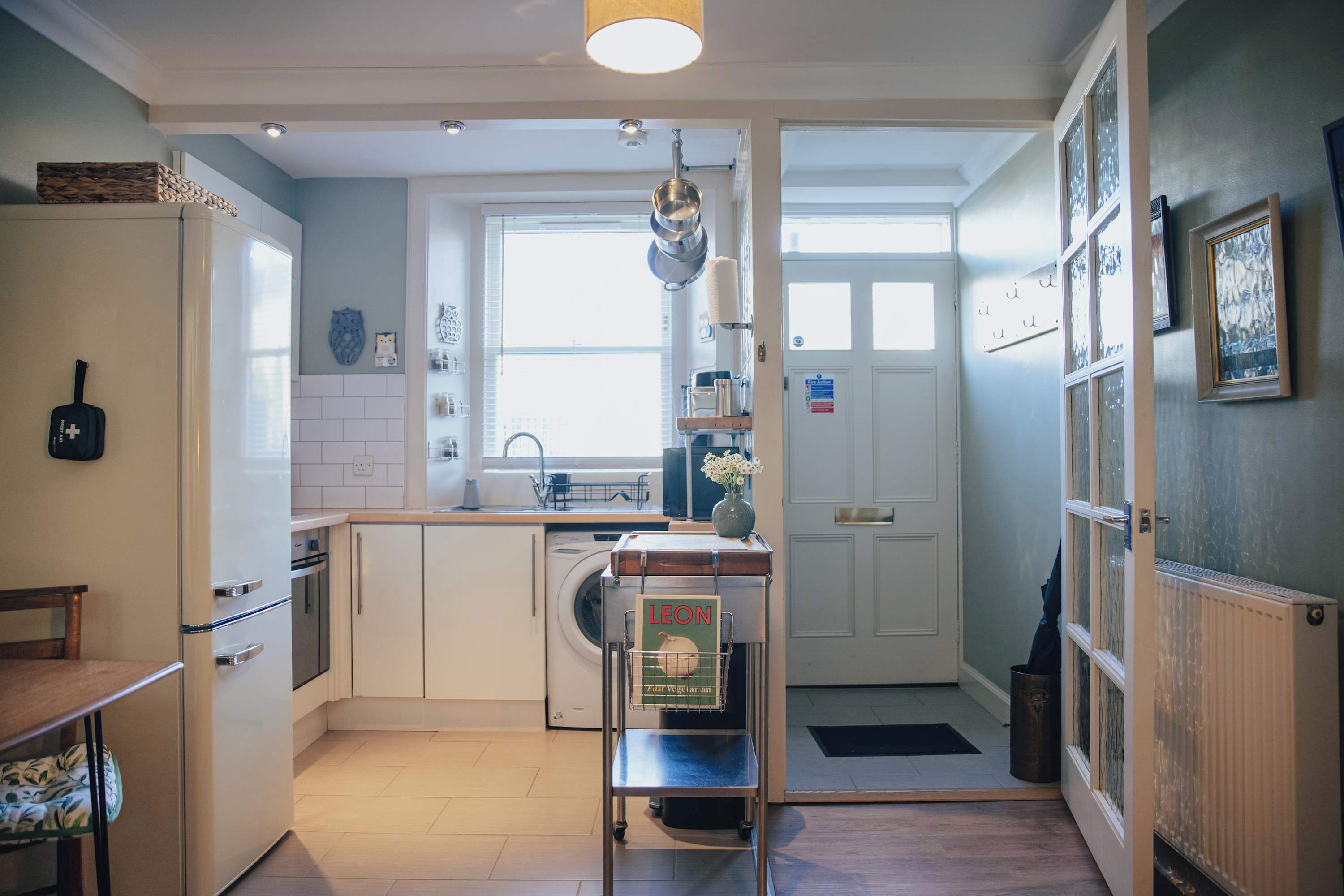 Une cuisine compacte comprenant un lave-linge, une petite table à manger et une étagère en métal avec un livre.