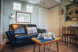Ein Wohnzimmer mit einer Ledersofa, einem Couchtisch mit Büchern, einer Lampe und einem Bücherregal.