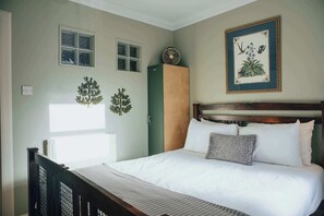 Ein ordentlich eingerichtetes Schlafzimmer mit einem hölzernen Kopfteil, einem Bett mit weißen Leinentüchern, einem grünen Kleiderschrank und zwei Fenstern an der Wand.