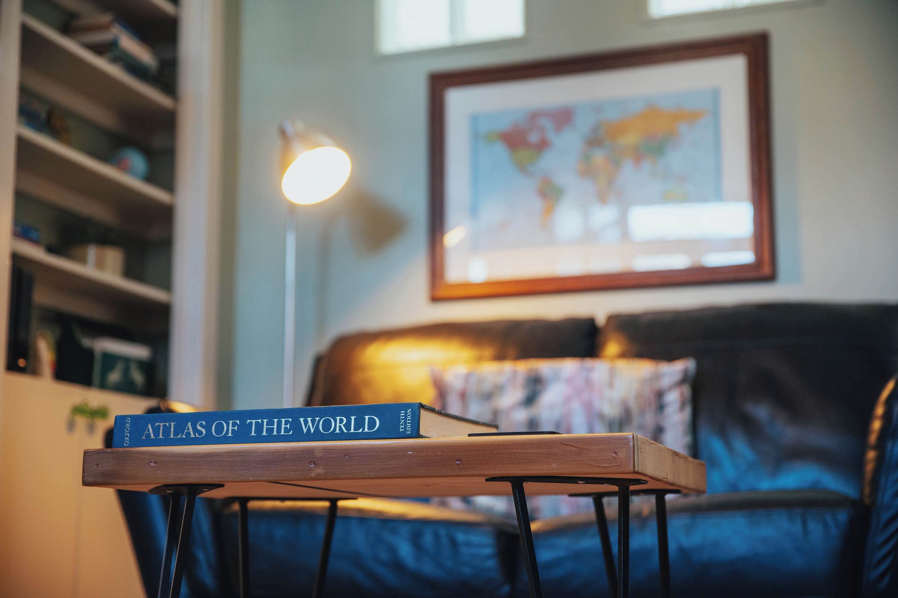 A book titled "Atlas of the World" on a wooden table in a room with a blue sofa and a map on the wall.
