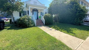 Una casa a due piani con un portico, un piccolo giardino anteriore e una strada di accesso.