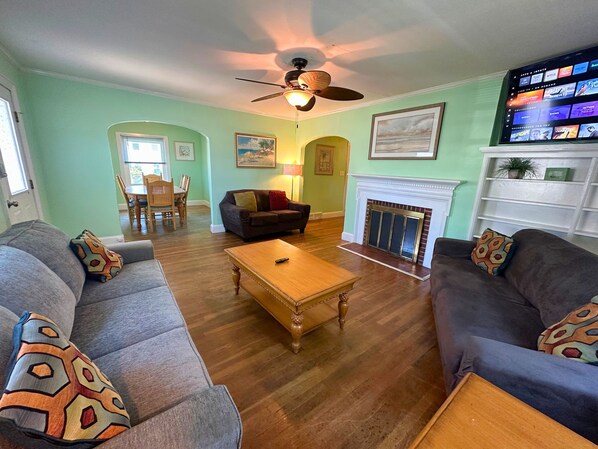 A living room with a fireplace, a ceiling fan, and a television displaying a streaming service. - Sleeps 18. Downtown - One Level Home - Short Walk To Beach (Ocean City)