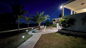 A nighttime view of a modern house with a well-lit garden, a pathway, and a view of the sea. - Bayview Resort, Blowing Point BEACHFRONT Villa with Stunning St. Maarten Views.  (Blowing Point)