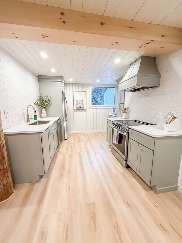 Cozinha moderna com piso de madeira, armários brancos e coifa de aço inoxidável.