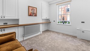 Een moderne keuken met witte kasten, een houten aanrecht en een radiator. Er is een raam met uitzicht op een bakstenen gebouw.