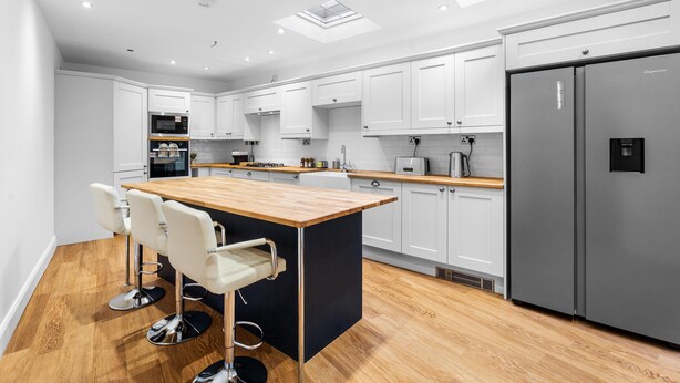 Een moderne keuken met witte kastjes, een centraal eiland, barstoelen, een roestvrijstalen koelkast en een dakraam.