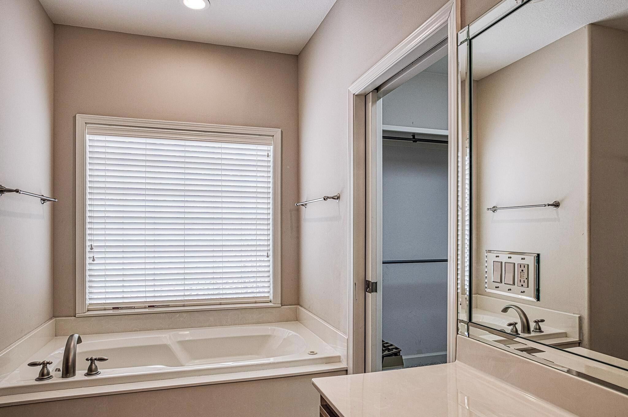 Une salle de bain avec une baignoire, une fenêtre avec des stores, un miroir et un dressing.