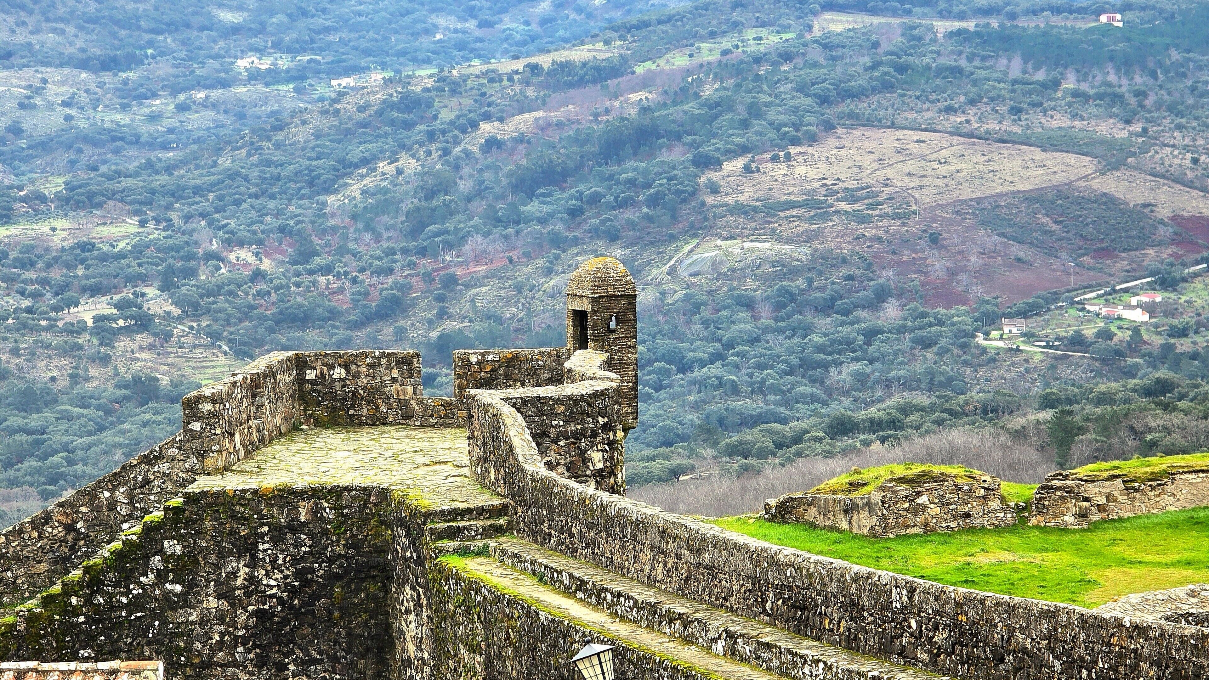 A stone fortress with a tower, surrounded by lush green hills and a valley.
