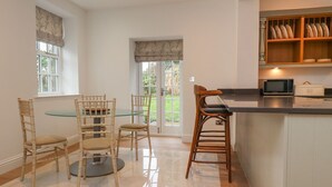 A kitchen with a glass dining table, two wooden chairs, a microwave, and a bread box. - The Lodge House (Lancaster)