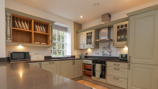 A modern kitchen with a large island, built-in appliances, and a window providing natural light. - The Lodge House (Lancaster)