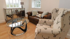 A living room with a glass coffee table, a brown leather sofa, and patterned armchairs. - The Lodge House (Lancaster)