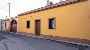 A yellow building with a brown door and windows, a paved street, and a utility pole. - Casa Terra Mia - Two Bedroom House, Sleeps 4 (Cabras)
