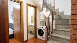 A laundry room with a washing machine, a wooden door leading to a bedroom, and a staircase with a stone handrail. - Casa Terra Mia - Two Bedroom House, Sleeps 4 (Cabras)