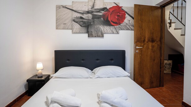 A hotel room with a bed, a nightstand with a lamp, a wooden door, and a staircase. - Casa Terra Mia - Two Bedroom House, Sleeps 4 (Cabras)