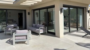 A modern outdoor living area with a glass-enclosed patio, white furniture, and a clear view of the adjacent room. - VILLA M, Swimming pool, Beach on foot (La Croix-Valmer)