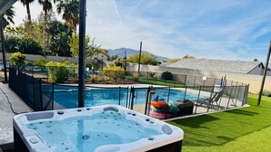 Un jacuzzi en un patio trasero con piscina, rodeado por una cerca y follaje.