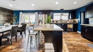 Una cocina moderna con una isla central, armarios oscuros y un comedor con mesa y sillas.