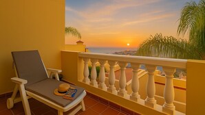 A balcony with a view of the sunset, a lounge chair, and a small table with a book and a hat. - Vacation Apartment 'Balcones Del Atlantico' with Sea View, Shared Pool and Wi-Fi (Playa de las Américas)