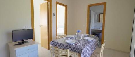 Un'area pranzo con un tavolo apparecchiato per due persone, una televisione su un mobile e uno specchio a parete.