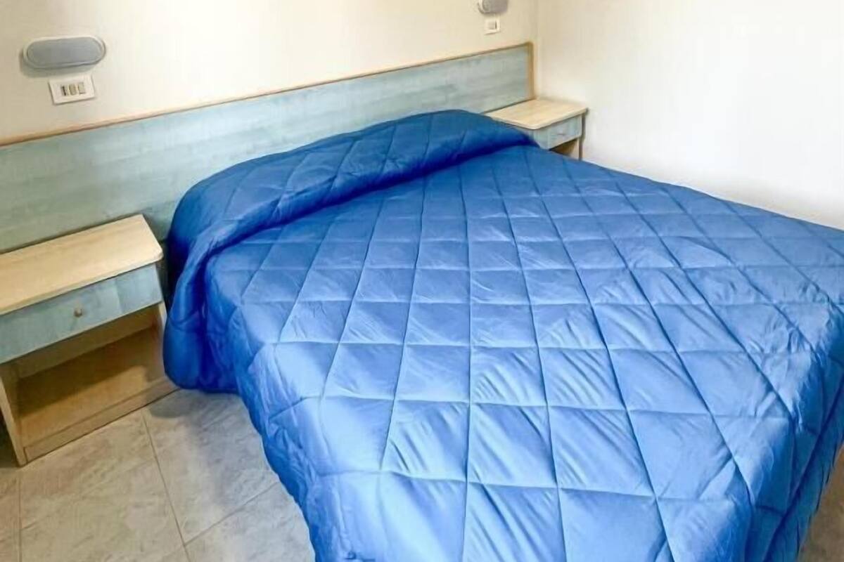 A bedroom with a bed, a nightstand, and a wall socket.