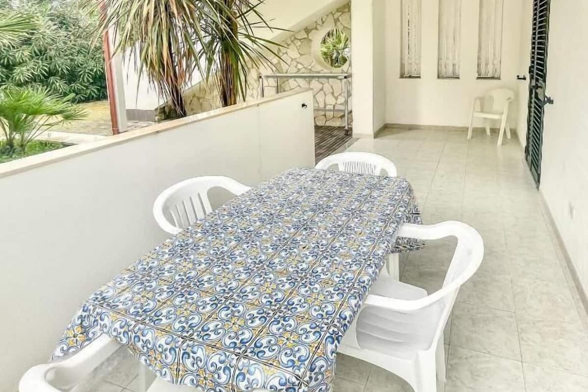A balcony with a tiled table and chairs, a potted plant, and a view of the garden.