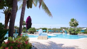 A pool area with palm trees, a staircase leading to a deck, and umbrellas. - Villaggio Merino (Vieste)