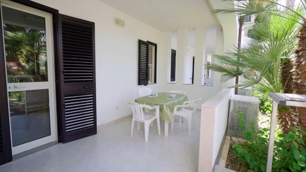 A covered patio area with a table and chairs, a sliding glass door, and a small garden area with plants.