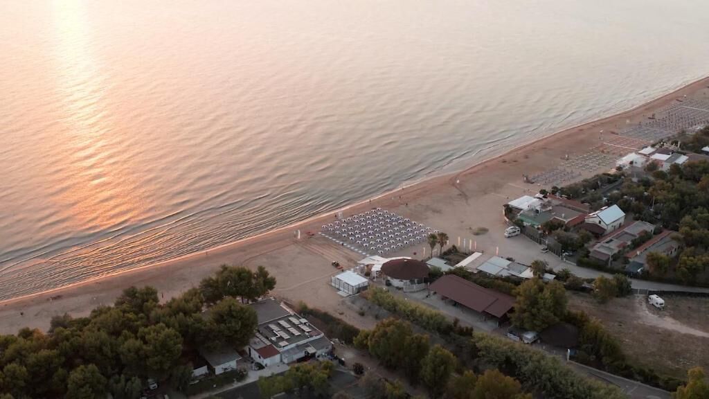 An aerial view of a coastal area with a beach, a row of buildings, and a parking lot.