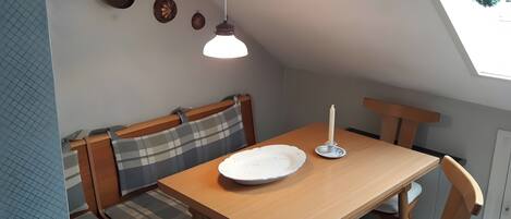 Un espace repas avec une table en bois, des bancs, une bougie et une suspension.