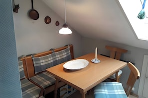 Ein Essbereich mit Holztisch, Bänken, einer Kerze und einer Pendelleuchte.