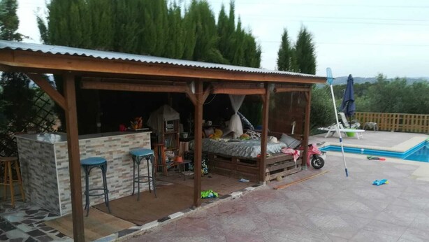 Een overdekt buitengebied met een bar, zitplaatsen, een zwembad en een houten constructie.