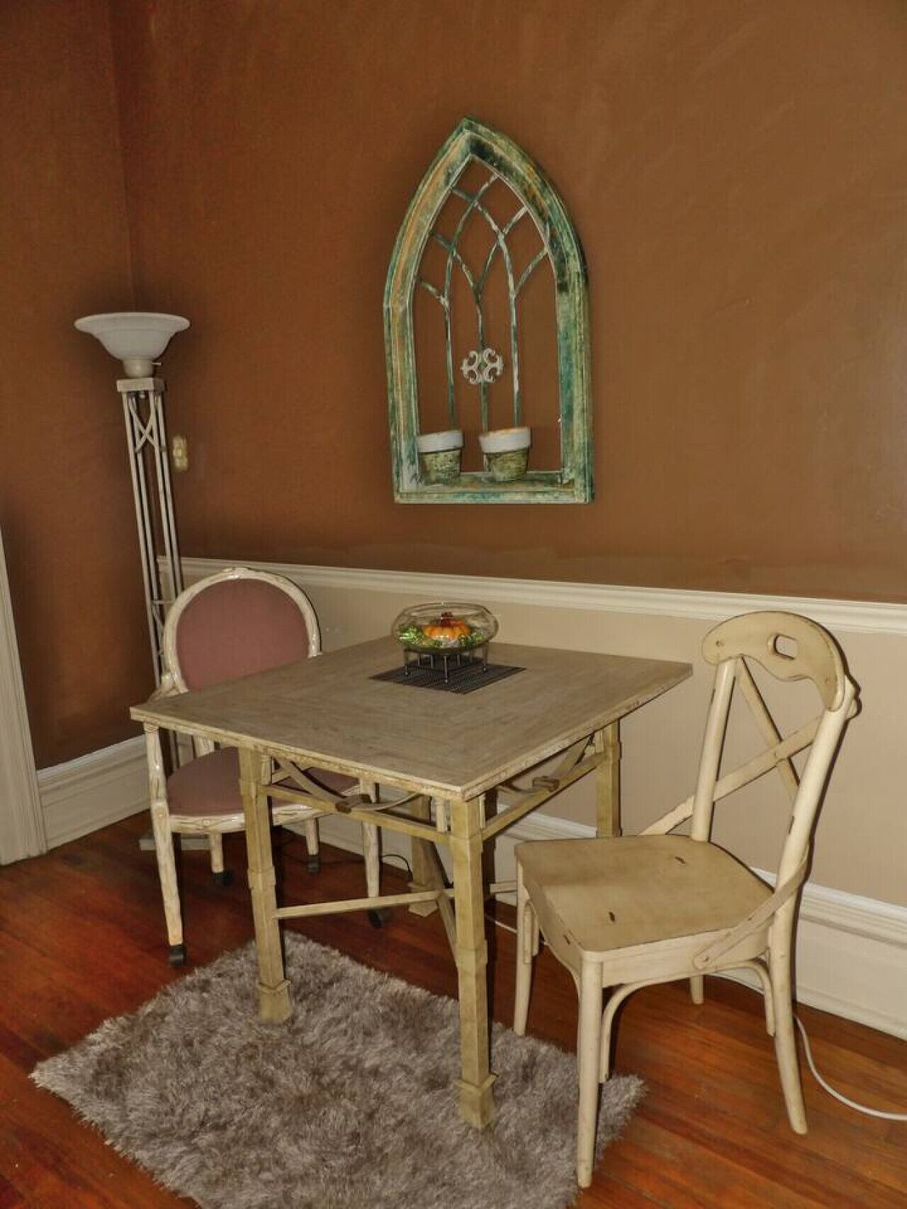 A dining area with a wooden table and two chairs, a decorative window, and a floor lamp.