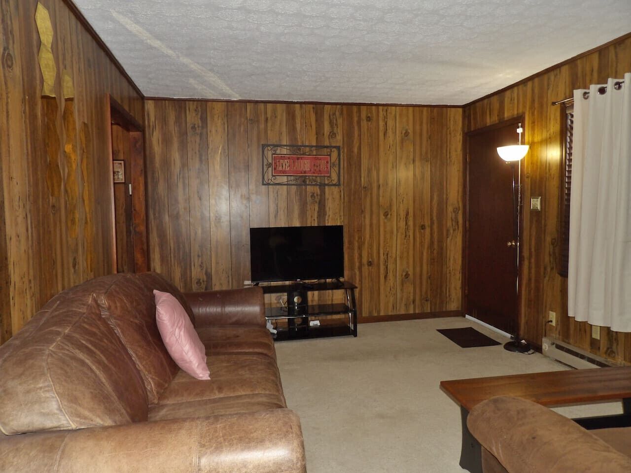 Una sala de estar con un sofá de cuero marrón, un televisor sobre un mueble de madera y una pared de madera con un letrero.