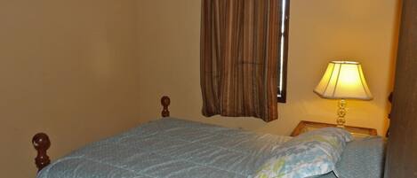 A bedroom with a bed, a nightstand, a lamp, and a window with curtains.
