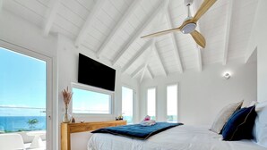 Ein Schlafzimmer mit einem großen Bett, einem Holztisch, einem an der Wand montierten Fernseher und einem Deckenventilator.
