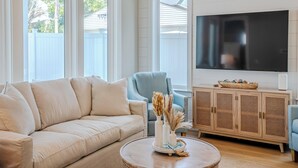 Een woonkamer met een beige bank, een blauwe fauteuil, een houten kast en een flatscreen televisie.