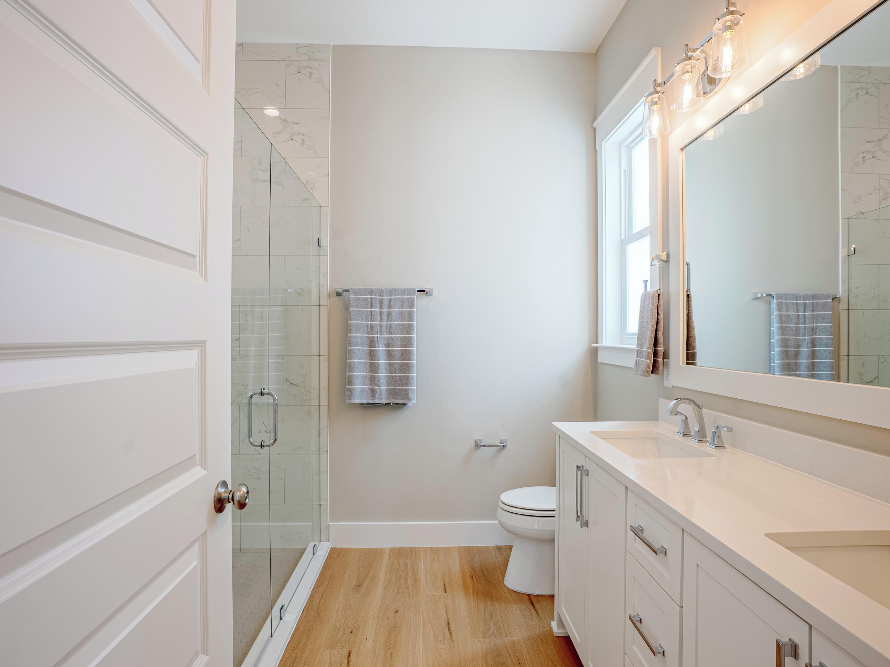 A modern bathroom with a glass shower enclosure, a toilet, and a vanity with a large mirror.