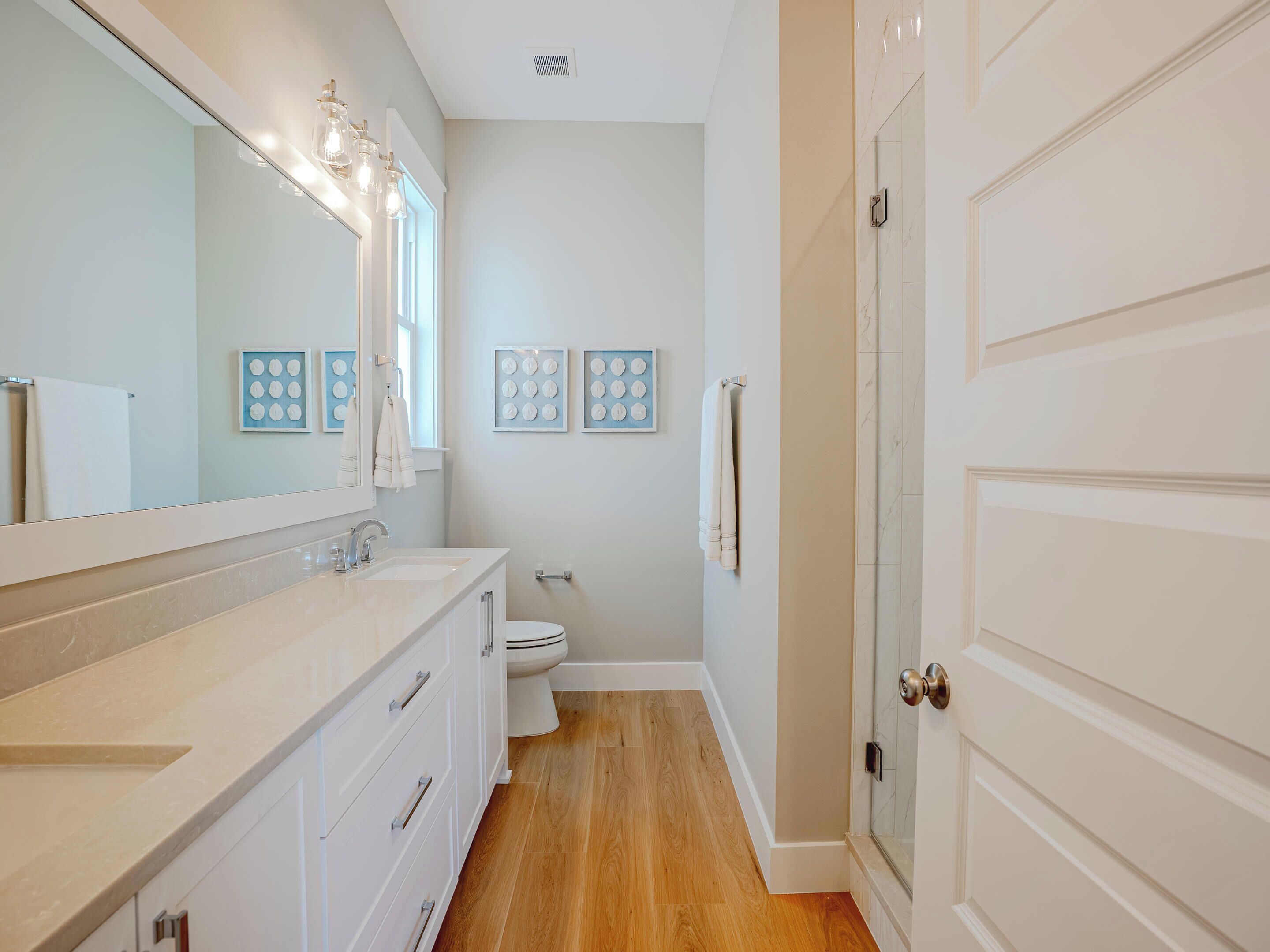 A modern bathroom with a large mirror, white fixtures, and a wooden floor.