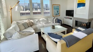 Een moderne woonkamer met een hoekbank, een glazen salontafel en een open haard.