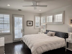 Ein Schlafzimmer mit einem Bett, Nachttischen, einem Deckenventilator und Fenstern mit Jalousien.