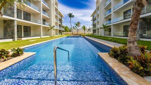 Une piscine entourée de bâtiments modernes dotés de balcons, de palmiers et surplombant un ciel dégagé.