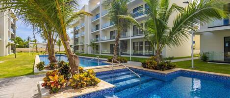 A modern hotel with a swimming pool, palm trees, and a well-maintained lawn.