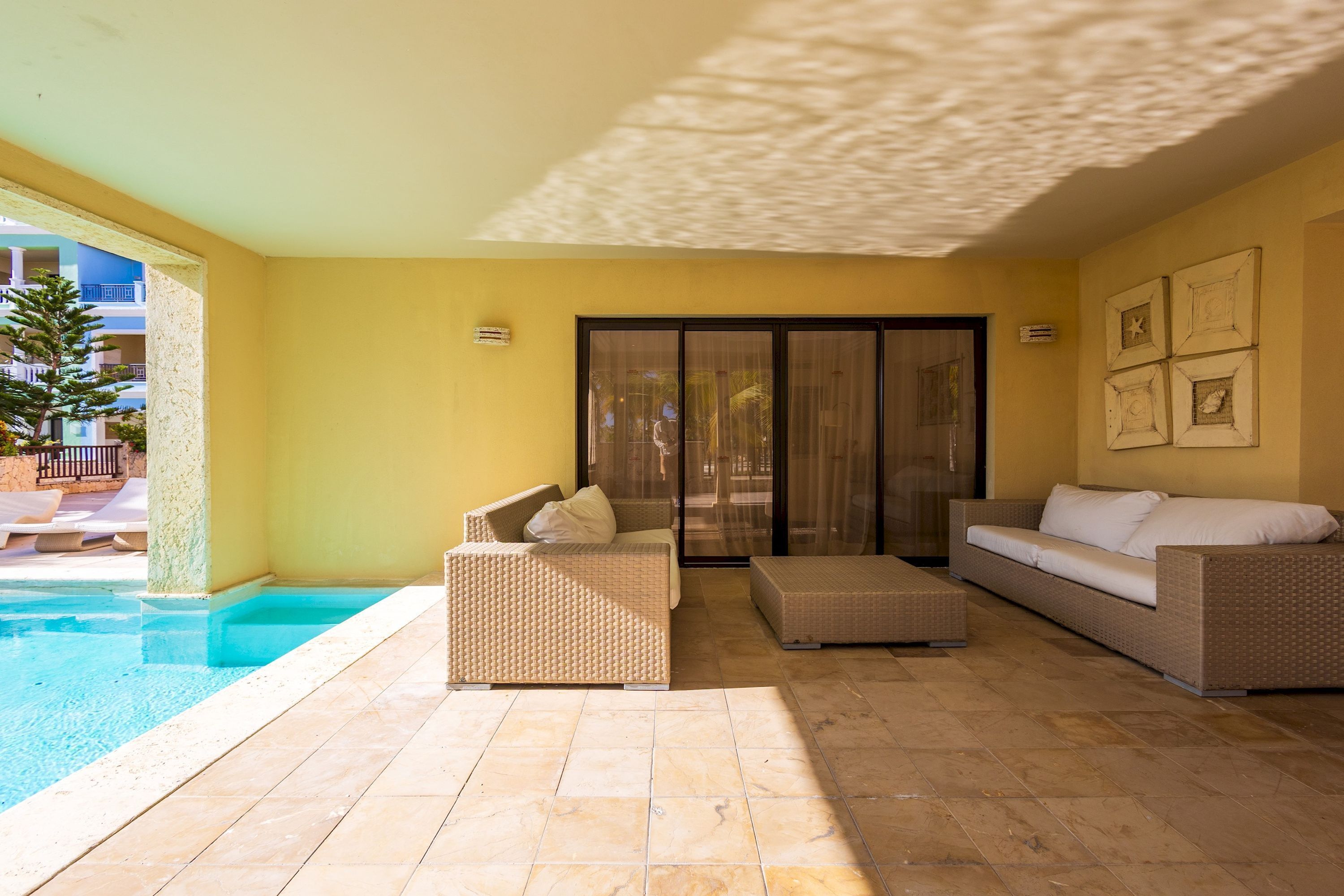A sunlit outdoor area with a pool, wicker furniture, and a sliding glass door leading to a balcony.