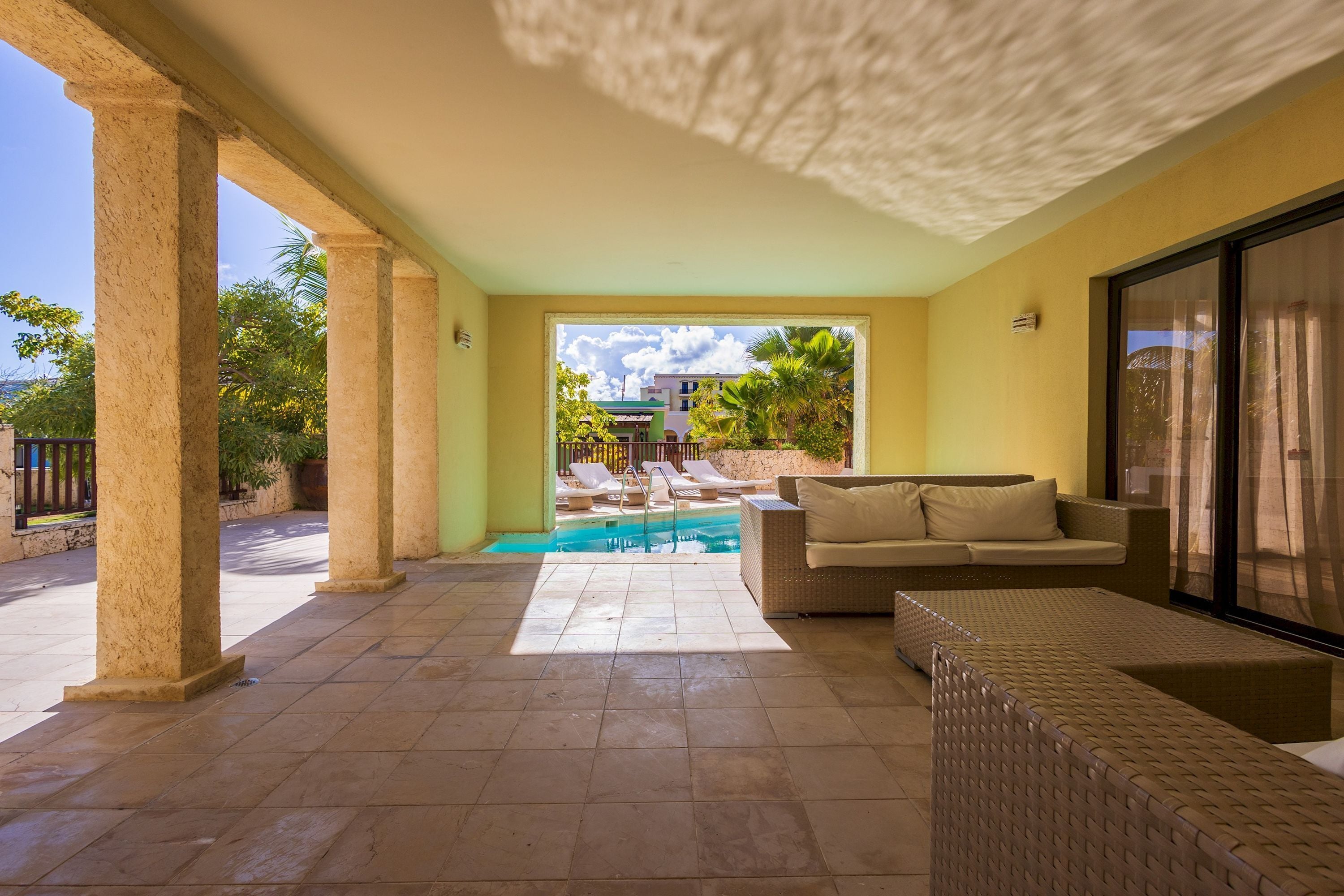 A covered outdoor area with a pool, lounge chairs, and a sofa.
