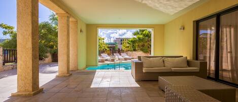 A covered outdoor area with a pool, lounge chairs, and a sofa.