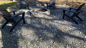 Un patio de grava con cuatro sillas Adirondack y un hogar de piedra.