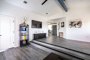 A spacious living area with a dark wood floor, a black entertainment unit, and a staircase leading to another level. - Big 6BR Beach Getaway for 20 | Near Ferry, 3 Units (Bolivar Peninsula)