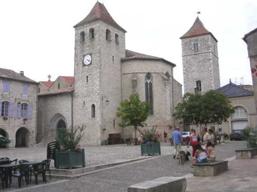 A historic stone building with a clock tower, a courtyard with seating, and people walking around.