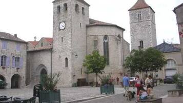 A historic stone building with a clock tower, a courtyard with seating, and people walking around.