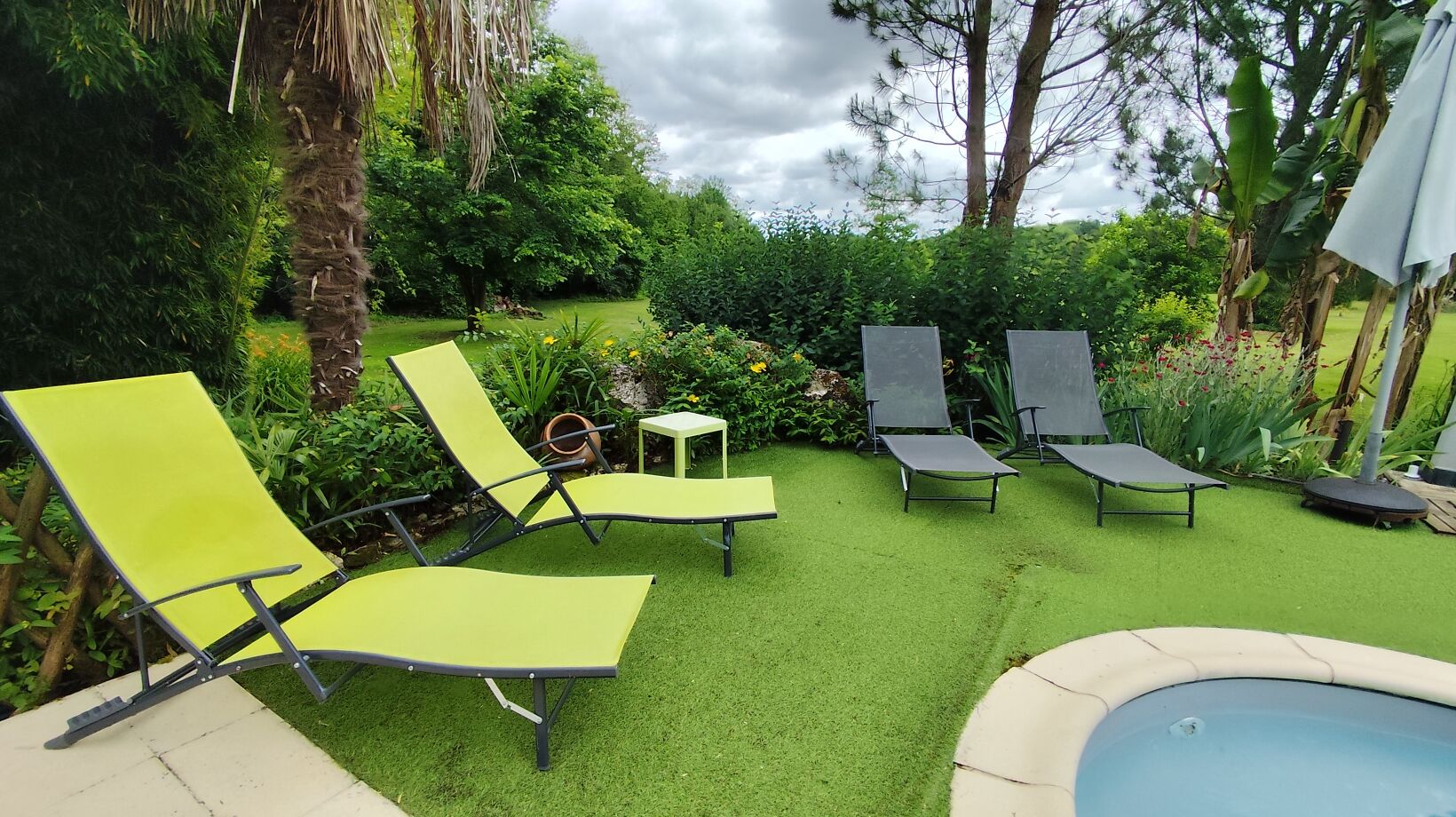 Un jardin avec une pelouse artificielle, une piscine et des chaises longues.